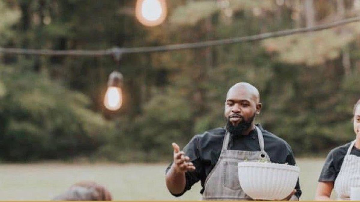 A chef presenting a dish at an outdoor farm dinner under string lights